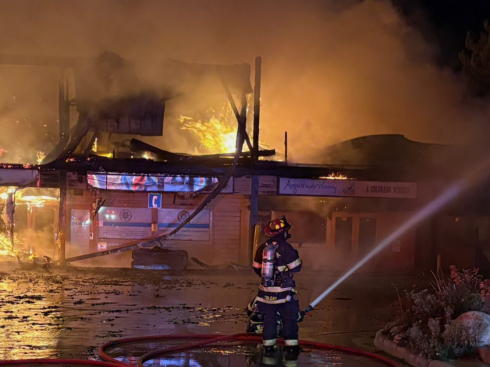 Firefighter directing a hose stream at a fully involved commercial building at night